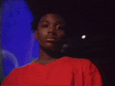 a man in a red shirt is sitting in front of a television with his eyes closed .
