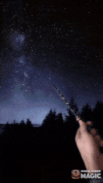 a person is holding a wand in front of a starry night sky with the words music video magic on the bottom right