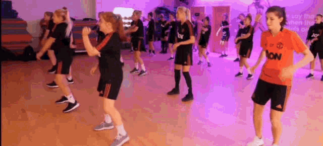 a group of young girls are dancing in a gym . one of the girls is wearing a jersey that says aon .
