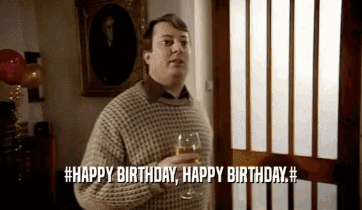 a man in a sweater is holding a glass of wine and says happy birthday