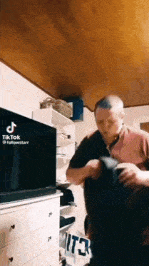 a man is holding another man in his arms in front of a television in a room .