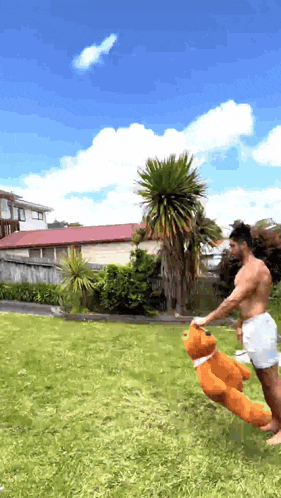 a shirtless man is holding a large teddy bear in a grassy yard