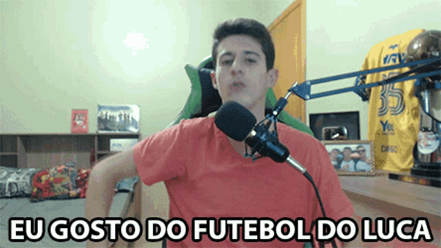 a young man in a red shirt stands in front of a microphone with the words eu gosto do futebol do luca below him