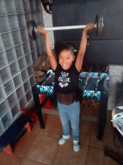a little girl lifting a barbell with a shirt that says rockstar