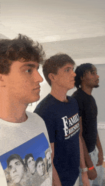 a man wearing a family friendly t-shirt stands in a line with two other men