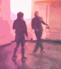 a man and a woman are dancing in a room with a pink wall