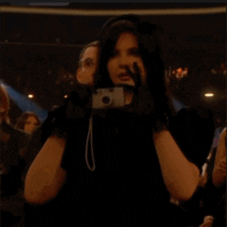 a man in a suit stands next to a woman in a black dress holding a cell phone