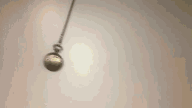a silver pocket watch is hanging from a chain on a white surface