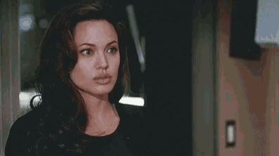a woman in a black jacket is standing in a dark room looking at the camera .