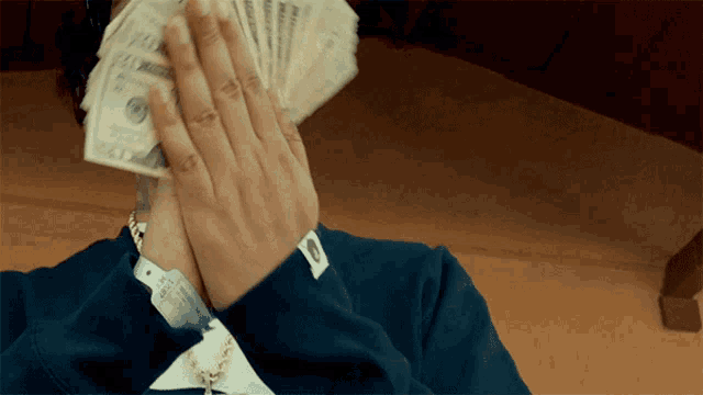 a person covering their face with a stack of money that has the number 100 on it