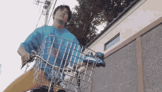 a man in a blue shirt is riding a bike with a basket on the front