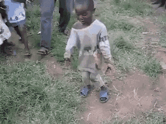 a young boy is dancing in a field with a crowd of people watching .