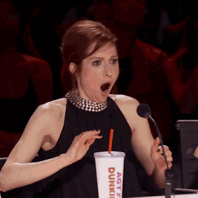 a woman in a black dress holds a dunkin ' donuts cup in front of a microphone