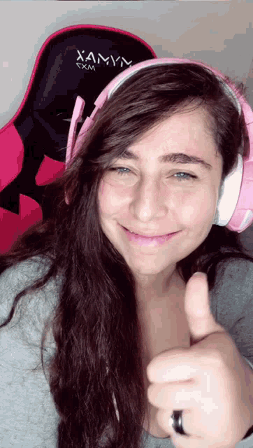 a woman wearing headphones giving a thumbs up in front of a chair that says xamn