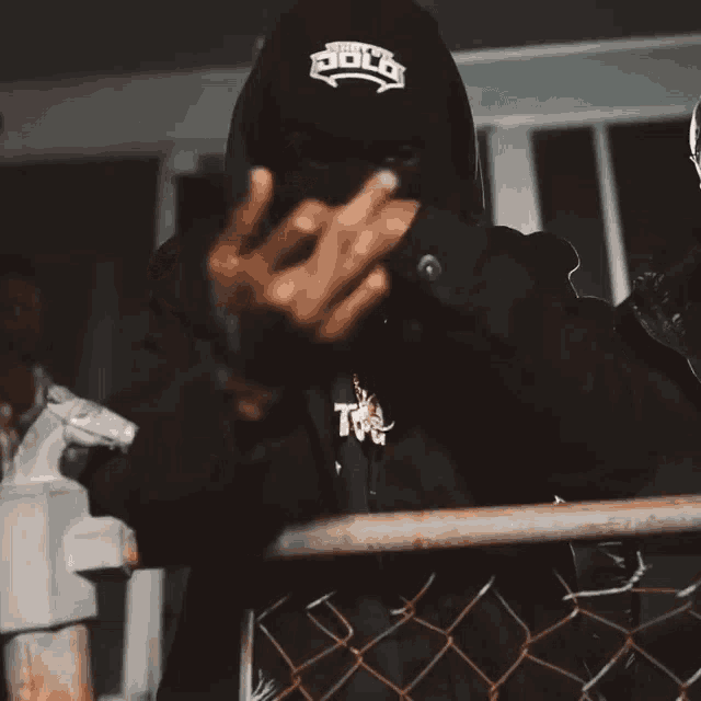 a person wearing a black hoodie with the word holt on it giving the middle finger
