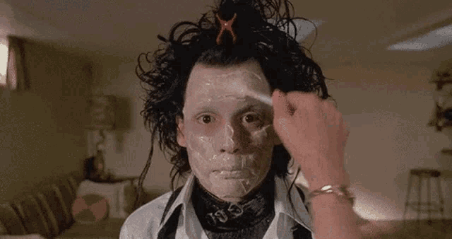 a person is applying makeup to a man 's face with a brush .