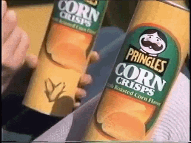 two cans of pringles corn crisps are being held in someone 's hands .
