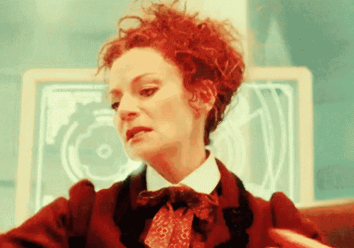 a woman with red curly hair is wearing a red coat and tie .