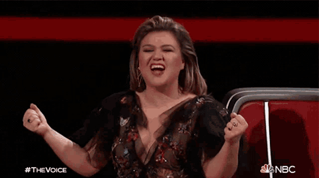 a woman in a black dress is screaming with her fist in the air and the words #thevoice nbc behind her