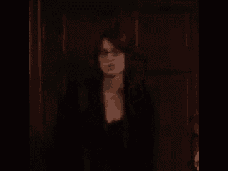 a woman in glasses is standing in front of a door in a dark room .