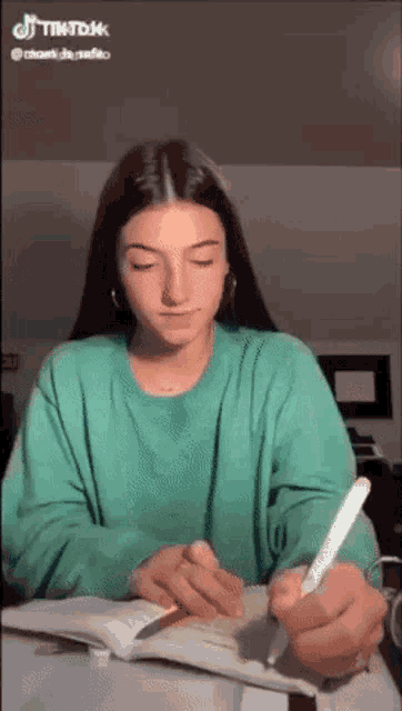 a girl in a green sweater is writing in a notebook with a pencil .