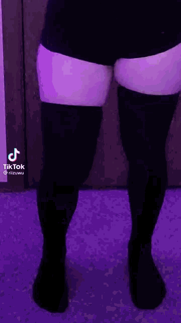 a woman wearing black shorts and black thigh high socks is standing in front of a purple door .