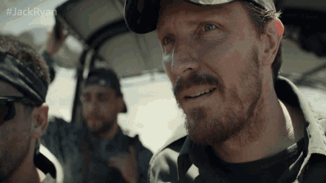 a man with a beard in a car with #jackryan written on the bottom right