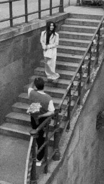 a black and white photo of a man holding a bouquet of flowers and a woman walking down a set of stairs
