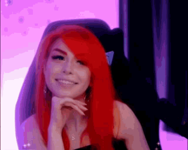 a woman with red hair is sitting in a gaming chair and smiling .