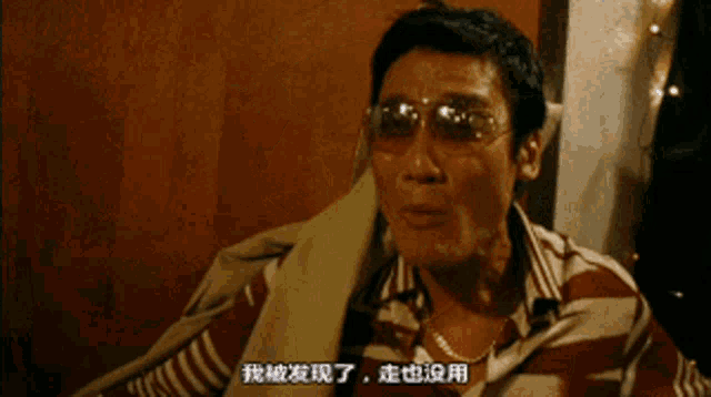 a man wearing sunglasses and a striped shirt has chinese writing on his shirt