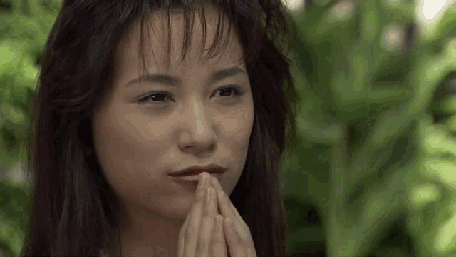 a close up of a woman with her hands folded in front of her face