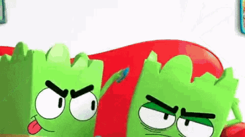 two green cartoon characters with angry faces are sitting next to each other .