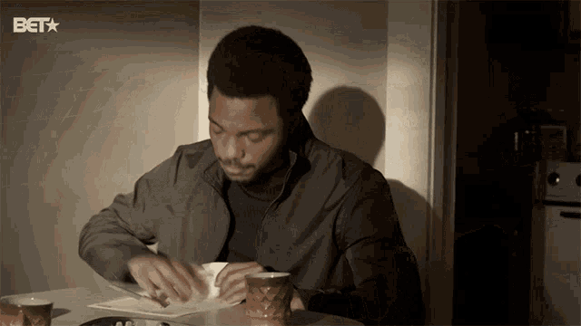 a man sits at a table with a bet logo on the bottom right