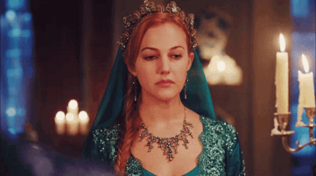 a woman in a green dress with a tiara on her head stands in front of candles
