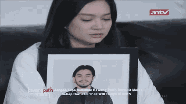 a woman is holding a picture of a man in front of an antv sign