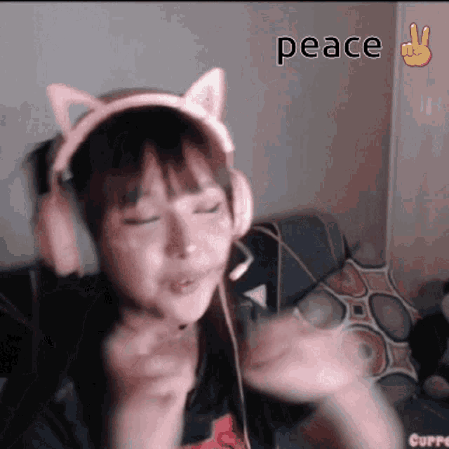 a girl wearing headphones with cat ears and a peace sign in the background