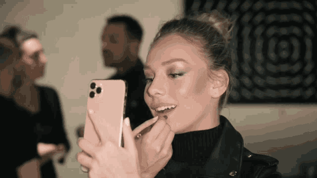 a woman is putting lipstick on her lips while looking at her phone