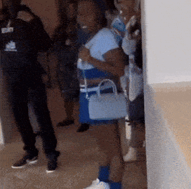 a group of people are standing in a room and a woman is holding a blue purse .