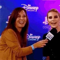 two women laughing in front of a disney channel banner