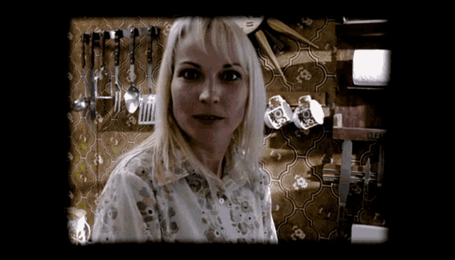 a woman stands in front of a wall with utensils hanging on it and a shelf that says ' off '