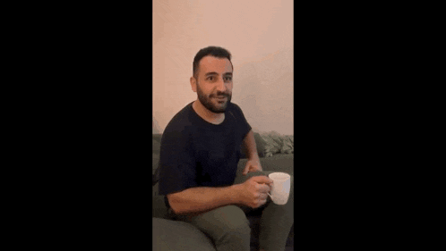 a man with a beard is sitting on a couch with a cup of coffee in his hand .
