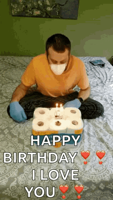 a man wearing a mask is sitting on a bed with a birthday cake made out of toilet paper