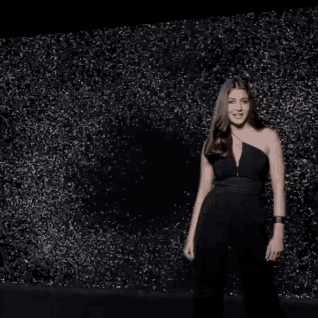 a woman in a black jumpsuit is standing in front of a wall of sparkles