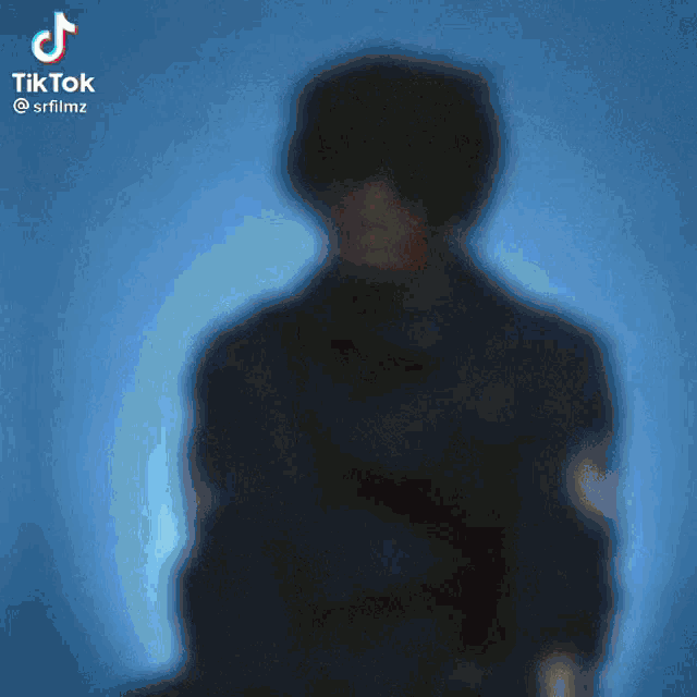 a blurry picture of a man in a black jacket and sunglasses against a blue background .