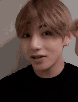 a close up of a young man with blonde hair wearing a black shirt .