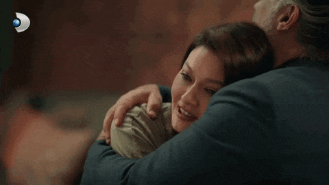 a man with a beard is hugging a woman in front of a sign that says ' televizyon ' on it