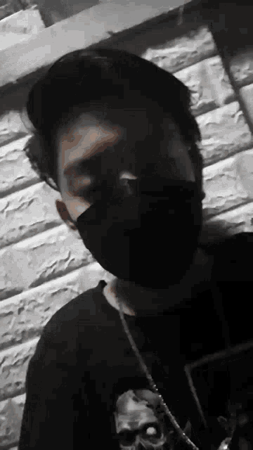 a young man wearing a black face mask and a skull necklace .