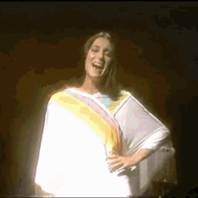 a woman in a white dress with a rainbow striped sleeve is standing on a stage .