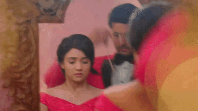 a man in a tuxedo and a woman in a red dress are looking in a mirror