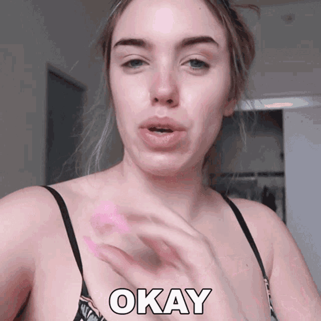 a woman in a bra is holding a pink object and the word okay is above her